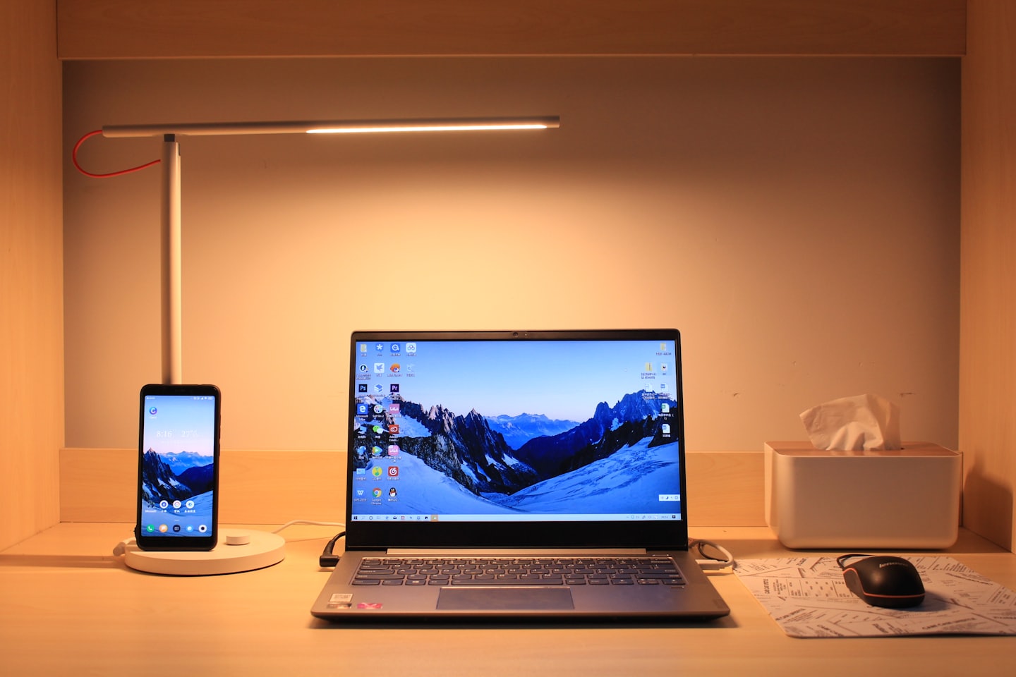 Laptop and smartphone charging on a wooden desk.
